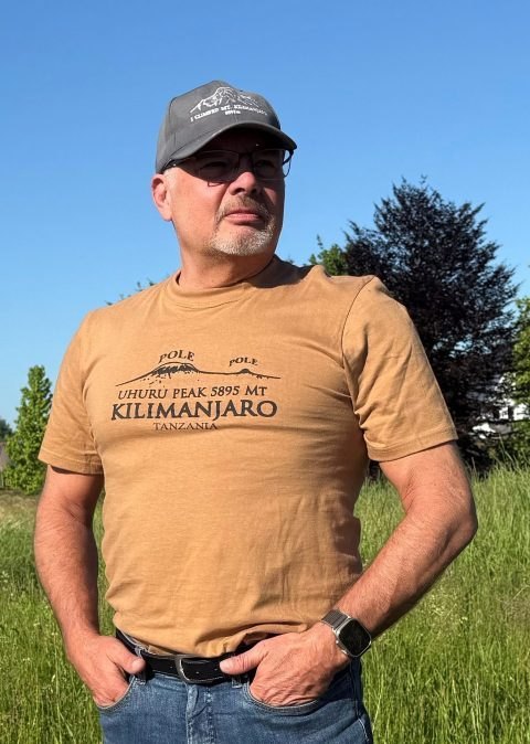 Jürgen Munz, Autor des Buchs Kilimanjaro, in einem T-Shirt mit Kilimanjaro-Aufdruck, mit Basecap und Sonnenbrille vor blauem Himmel