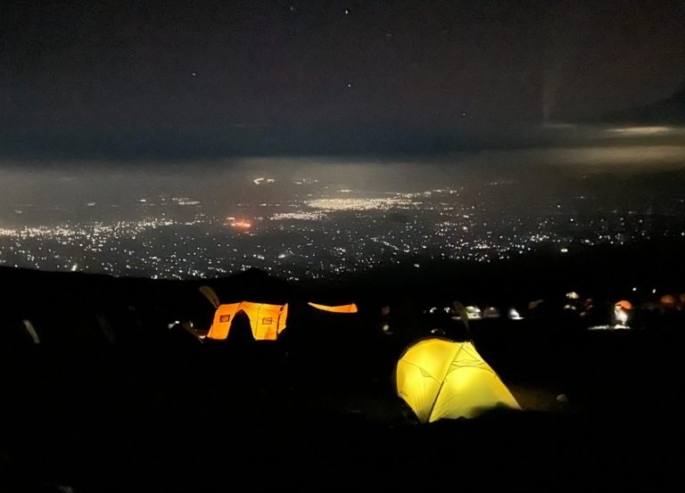 Nachtlager: ein leuchtendes gelbes Zelt, unten die Lichter der Stadt